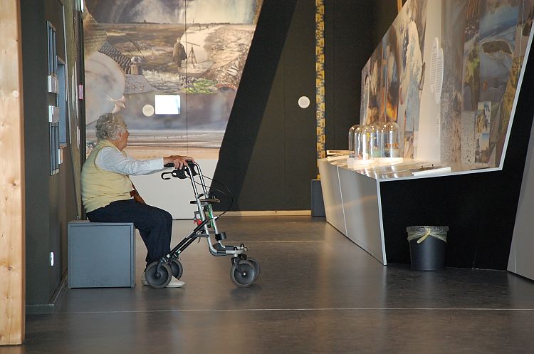 Alte Dame mit Rollator vor einer Theke im Wattenmeer Besucherzentrum