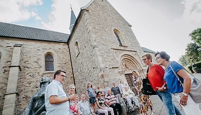 Eine Touristengruppe vor einer Kirche hört einem Gästeführer zu 
