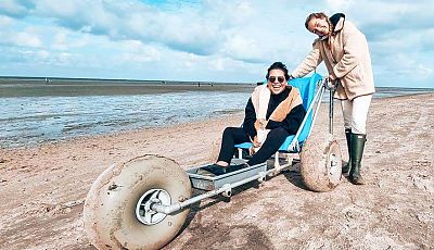 Zwei fröhliche Mädchen, eines davon sitzt auf einem Wattmobil, um das Wattenmeer barrierefrei zu erkunden