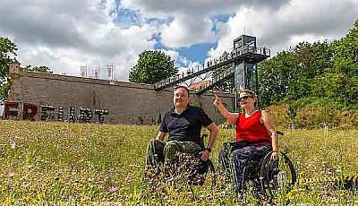 Zwei Rollstuhlfahrer zeigen zum Aufzug auf den Petersberg